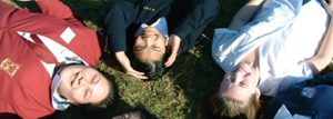 Female students laying on grass looking up at camera