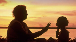 Aboriginal woman clapping hands with aboriginal child at sunset