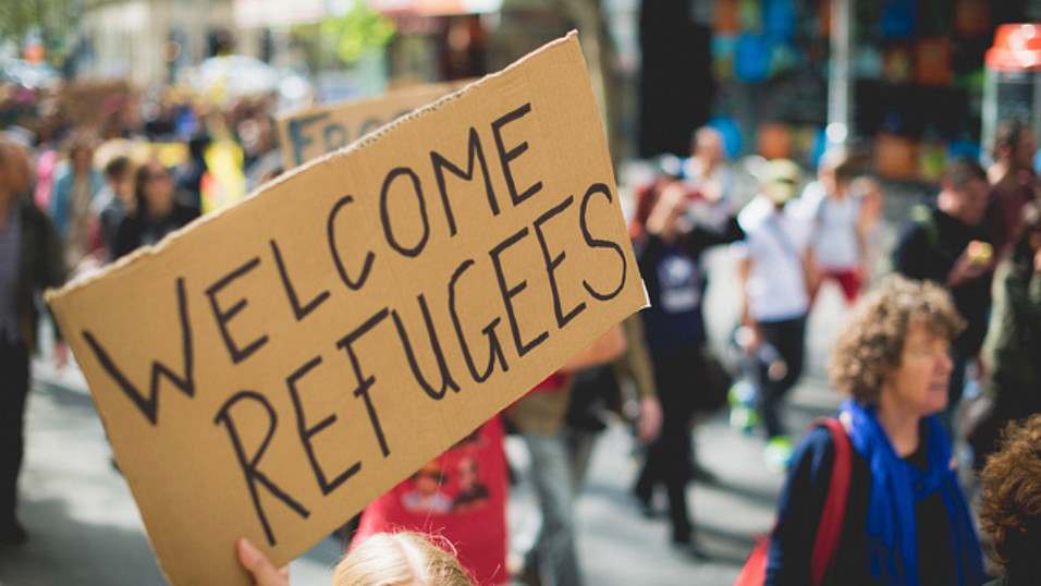 Marching people carrying a sign - Welcome Refugees