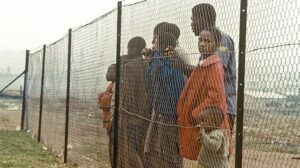 Children behind fence that separates them from the white community near Johannesburg during time of apartheid in South Africa.