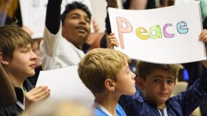 Boy in crowd holding 'Peace' sign