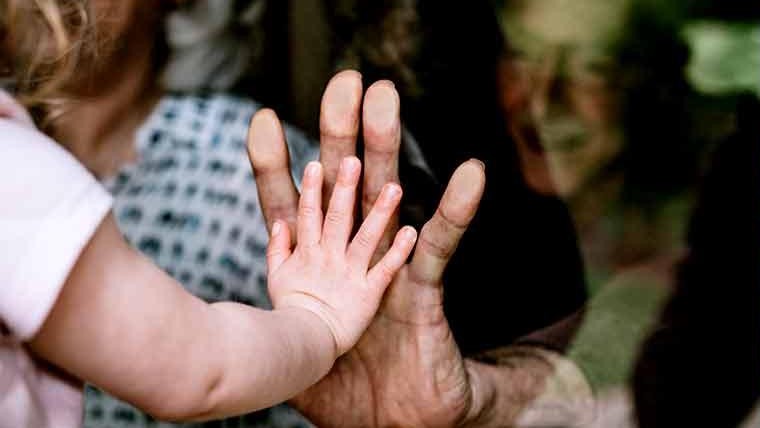 child and adult touching hands through a glass pane