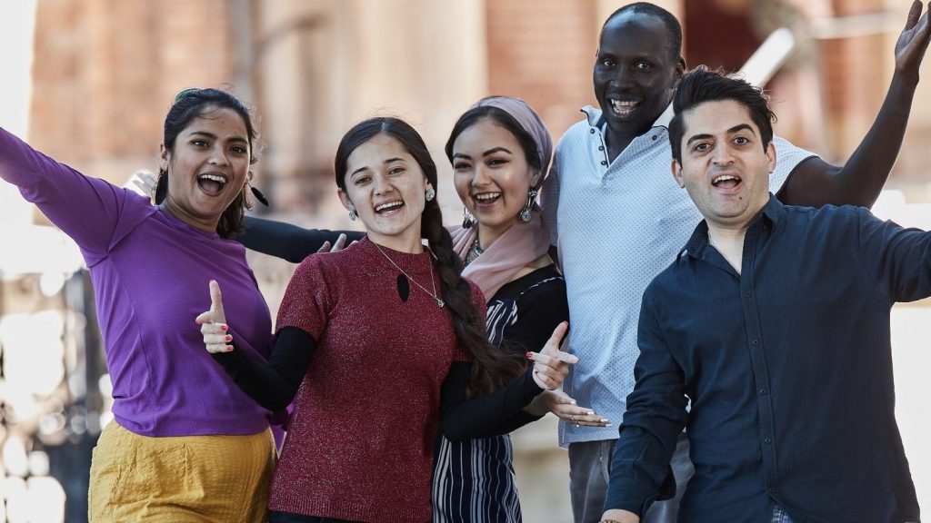 Three women and two men from culturally and linguistically diverse backgrounds smiling and posing for the camera.
